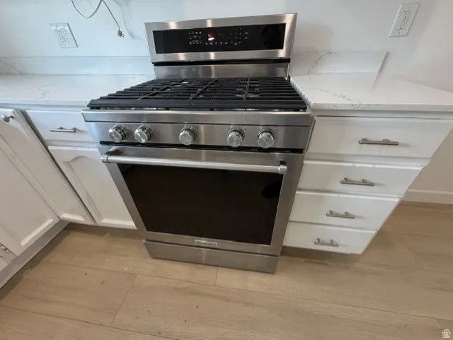 Stainless steel range with gas cooktop, white cabinetry, polished drawer pulls, and light-toned wood-finish flooring