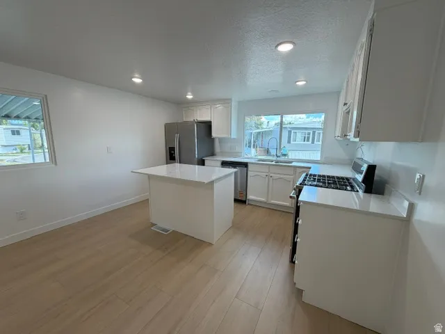Modern kitchen featuring light wood-finish flooring, white cabinetry, a center island with a stone countertop, and recessed lighting