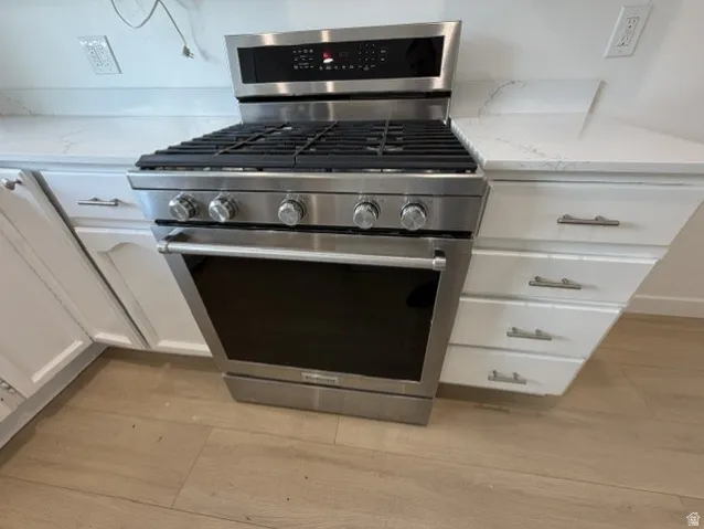 Stainless steel range with gas cooktop, white cabinetry, polished drawer pulls, and light-toned wood-finish flooring