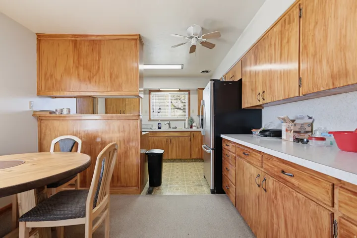 Wood cabinetry, solid surface countertops, stainless steel refrigerator, ceiling fan, and built-in wood divider