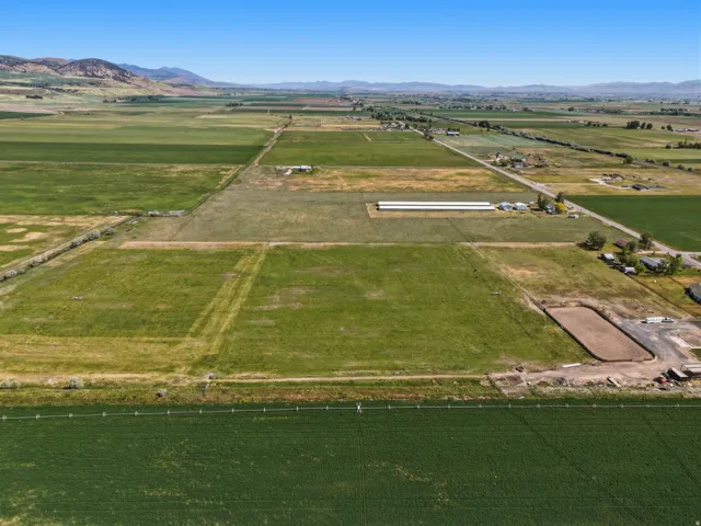 Expansive agricultural land featuring a clear blue sky, distant mountains, cultivated fields, and a visible equestrian arena