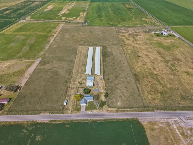 Expansive agricultural property featuring multiple structures, two long outbuildings, a primary residence, and a paved road frontage