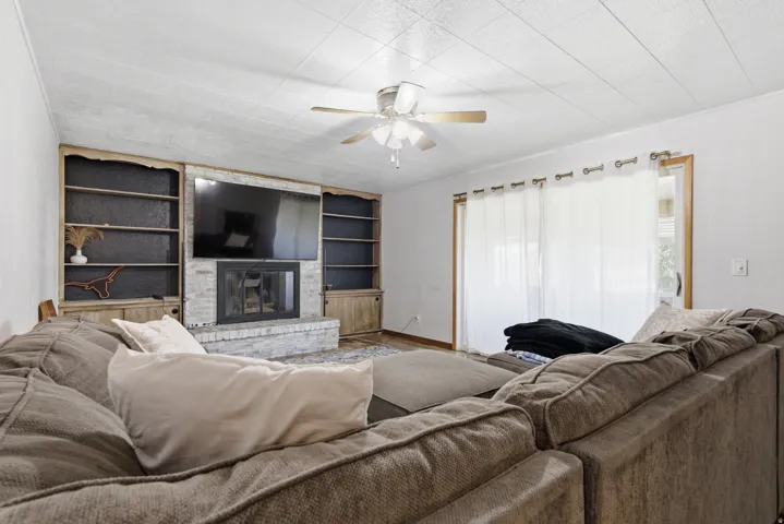 Built-in shelving flanking a stone-clad fireplace, wood-finish flooring, and a ceiling fan