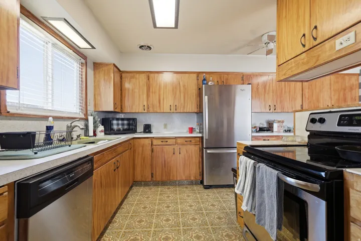 Kitchen featuring wood-finish cabinetry, stainless steel appliances, patterned flooring, and a window above the sink