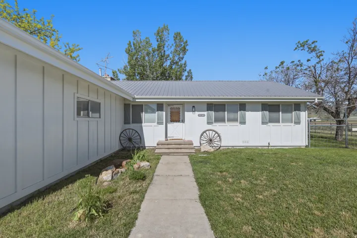 White exterior siding with a gray metal roof, featuring a concrete pathway and steps to the entrance