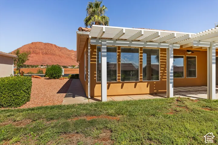 Terracotta-tiled roof, multiple large windows, attached pergola, stucco exterior, and red rock mountain backdrop