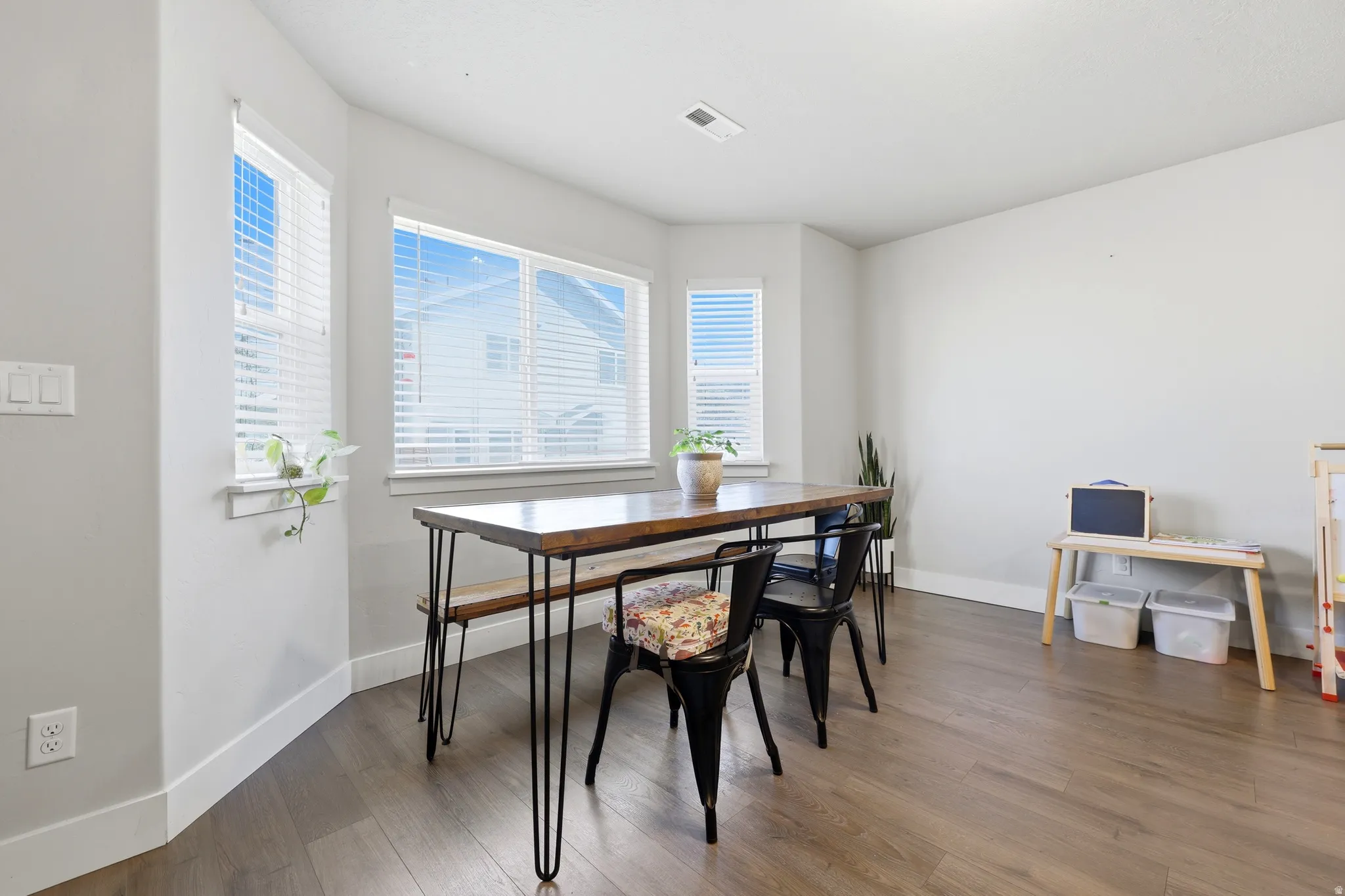 Wood-finish flooring, white trim, multiple windows with white blinds, light gray wall color, and a ceiling-mounted light fixture