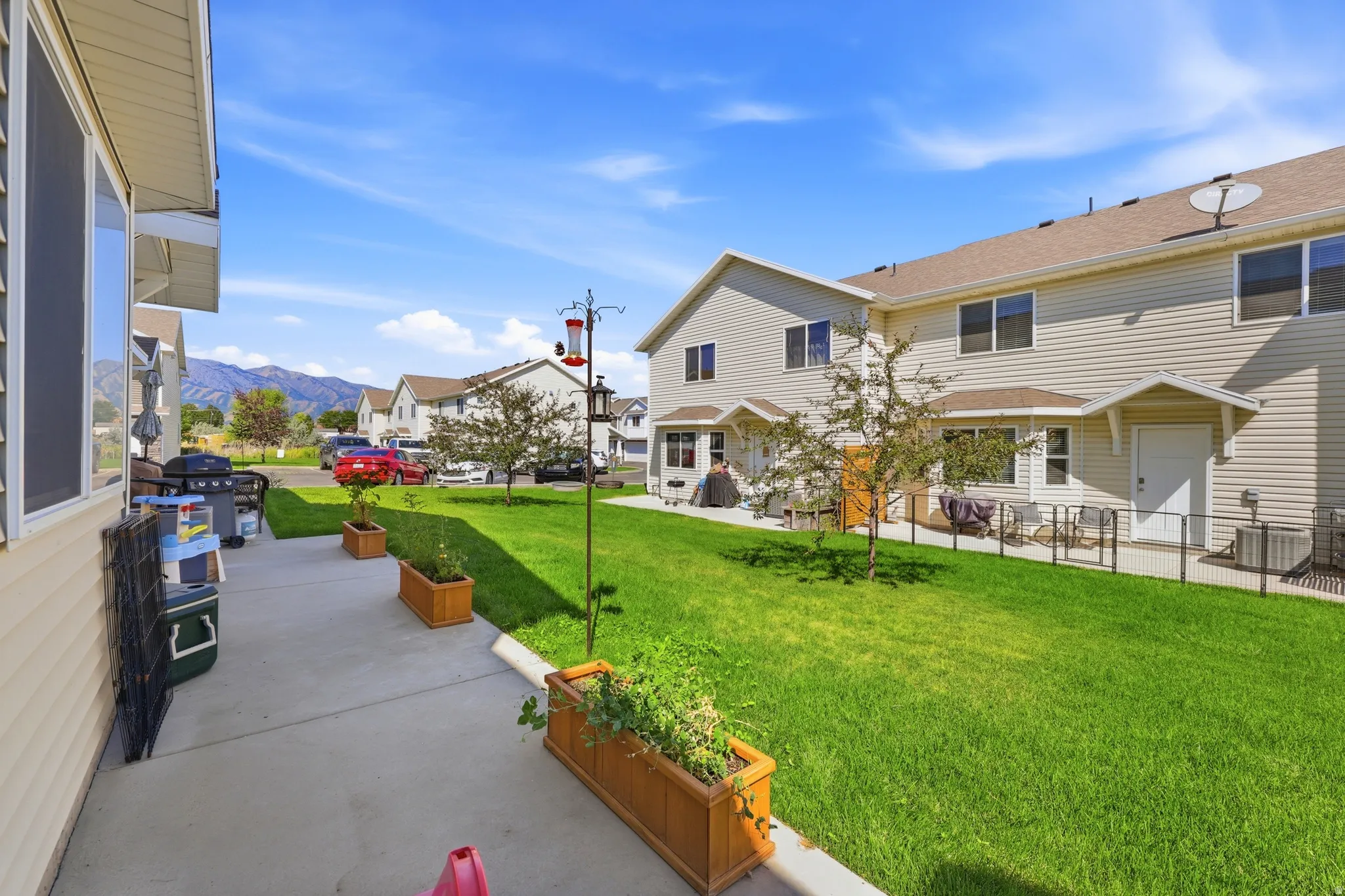 Expansive green lawn with mountain backdrop, concrete patio, and built-in planter boxes