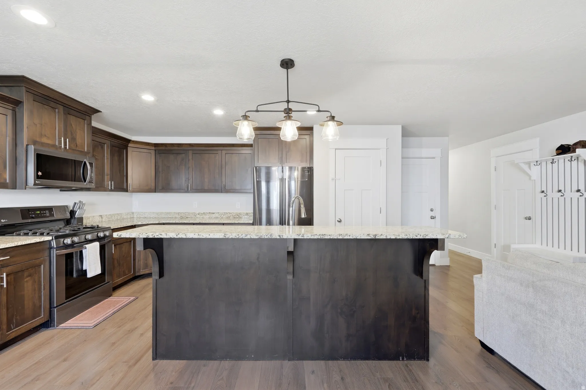 Spacious kitchen featuring an island with built-in sink, dark wood-finish cabinetry, stainless steel appliances, and wood-finish flooring