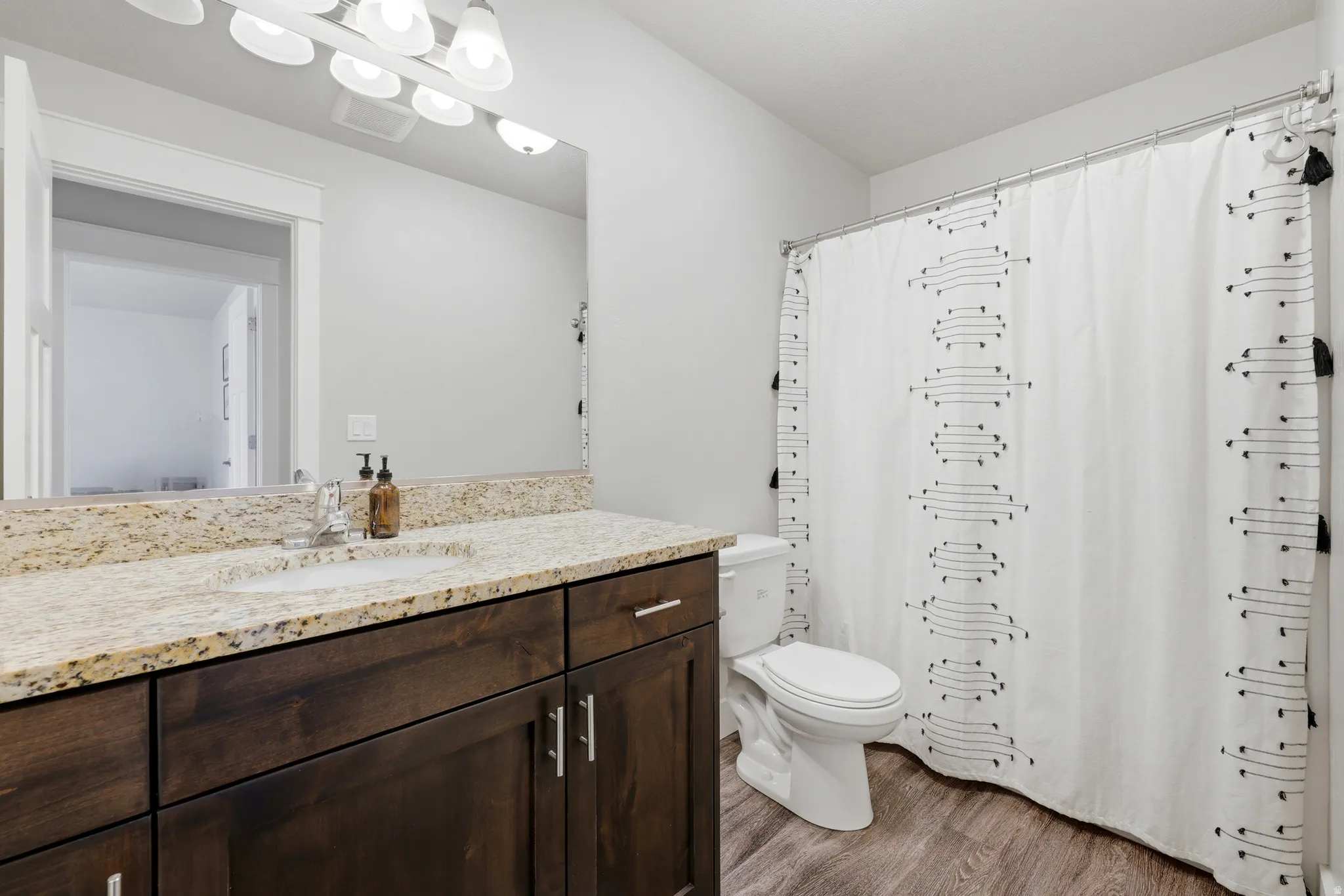 Vanity with an integrated sink, granite-style countertop, dark wood-finish cabinetry, and wood-finish flooring