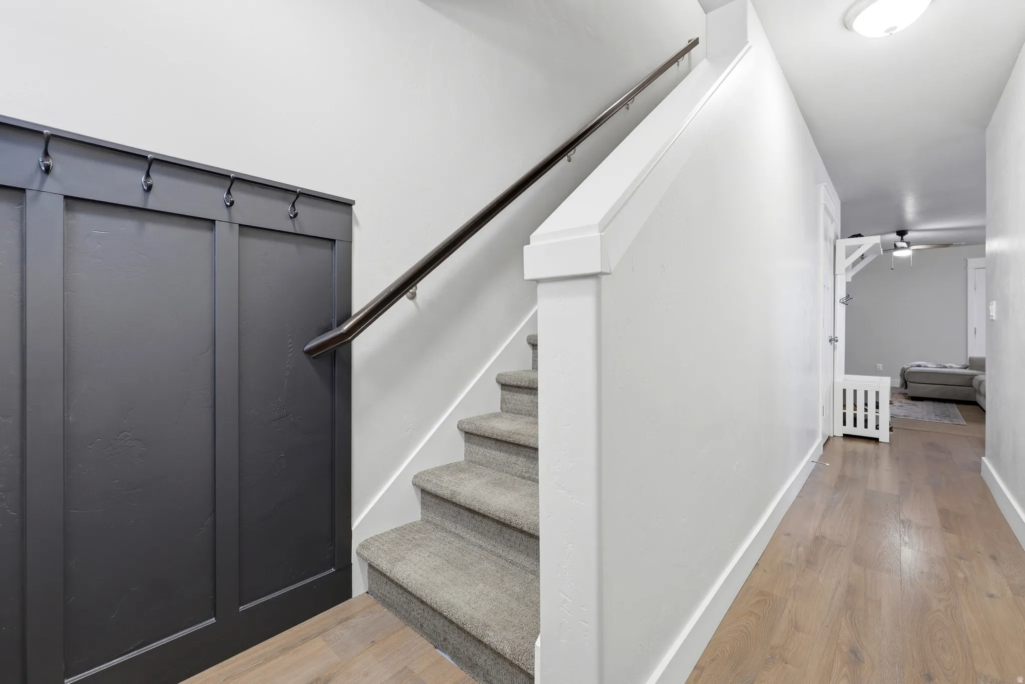 Hardwood-finish flooring, carpeted stairs, dark paneling with integrated hooks, and a white handrail