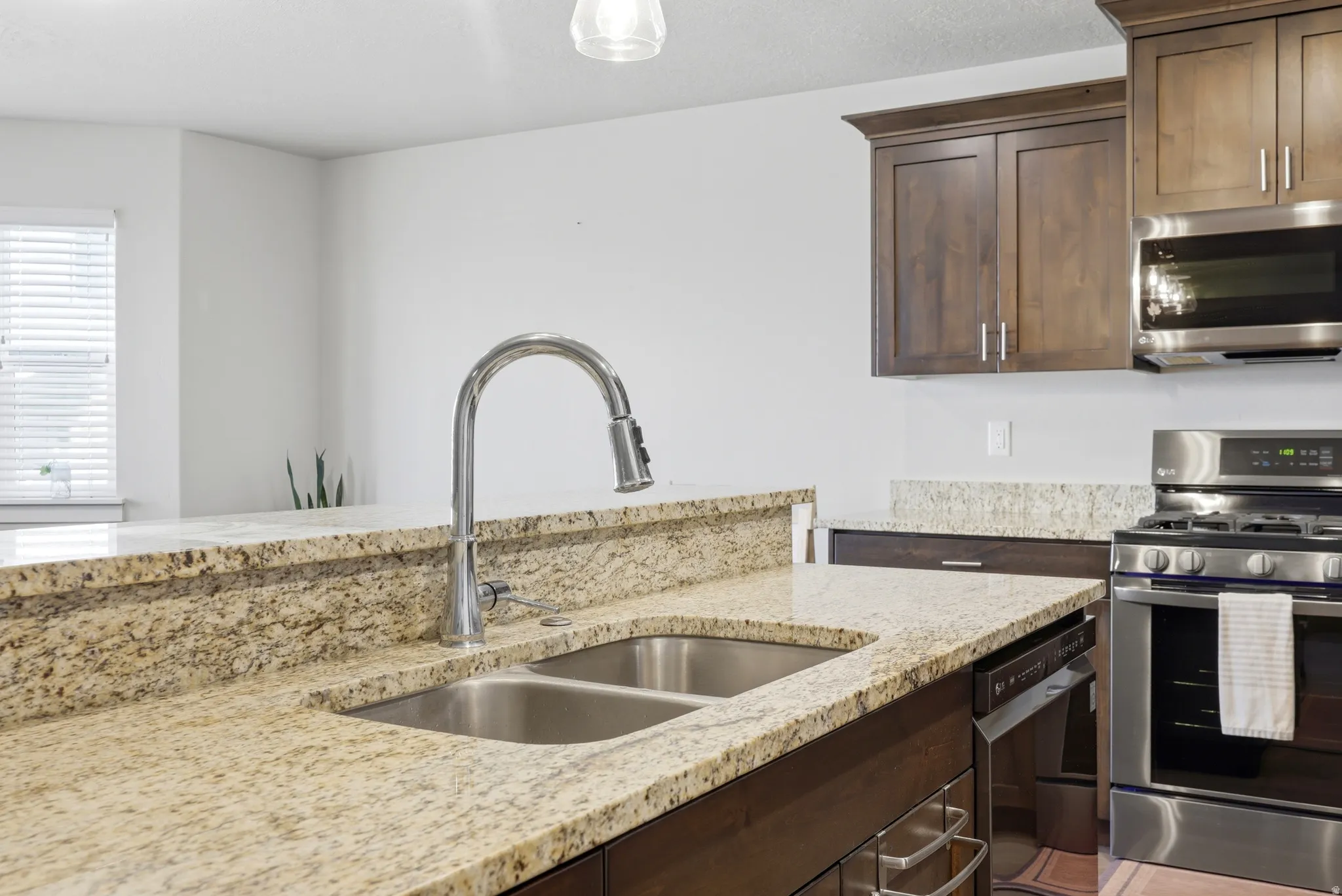 Kitchen featuring a double basin stainless steel sink, pull-down faucet, granite countertops, wood-finish cabinetry, and stainless steel appliances