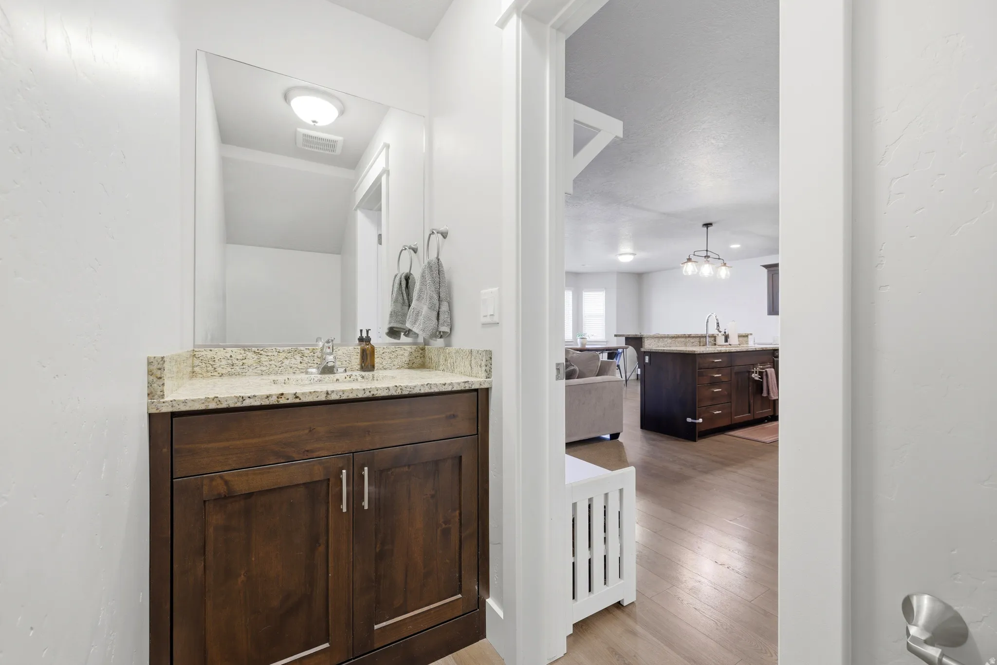 Wood-finish flooring, dark wood vanity, light-colored countertop, and a contemporary light fixture
