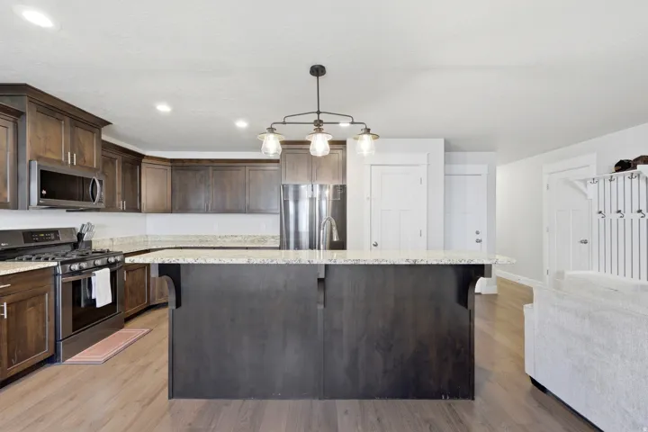 Spacious kitchen featuring an island with built-in sink, dark wood-finish cabinetry, stainless steel appliances, and wood-finish flooring