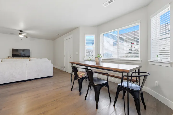 Spacious living area featuring wood-finish flooring, ample natural light from multiple windows, and a ceiling fan
