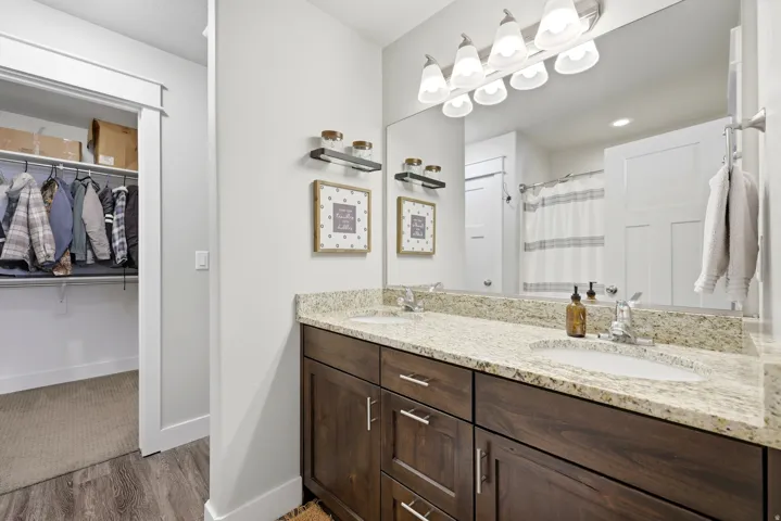Dual vanity with granite countertop, wood-finish cabinetry, and contemporary light fixture