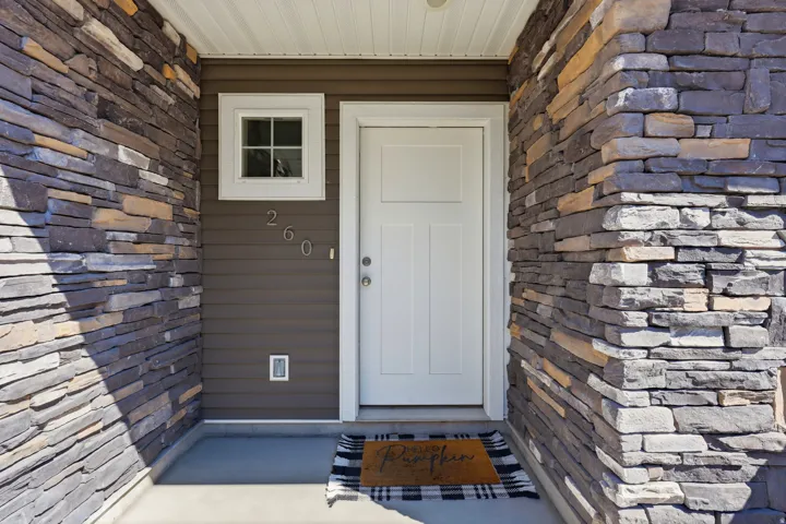 Stone veneer and horizontal siding exterior featuring a white entry door, an upper transom window, and a concrete entry pad