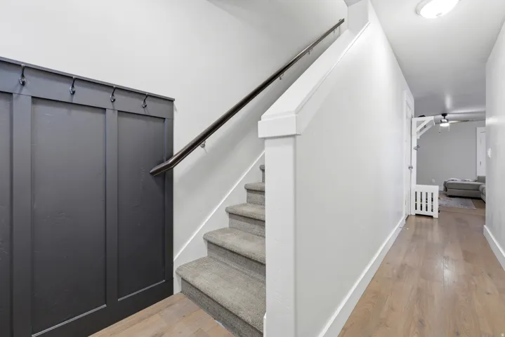 Hardwood-finish flooring, carpeted stairs, dark paneling with integrated hooks, and a white handrail