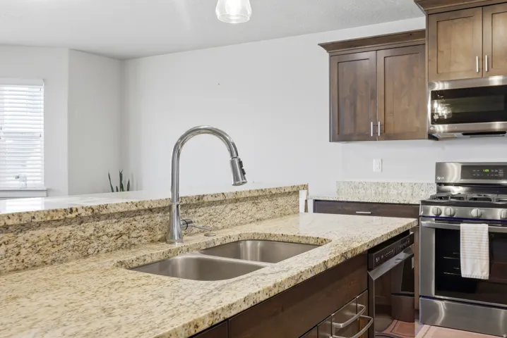 Kitchen featuring a double basin stainless steel sink, pull-down faucet, granite countertops, wood-finish cabinetry, and stainless steel appliances