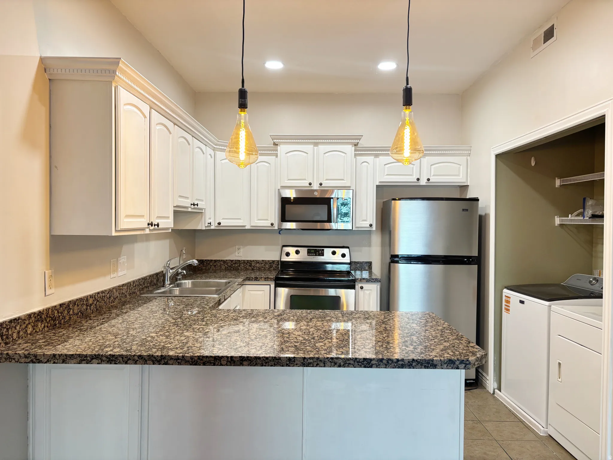 Kitchen featuring white cabinetry, stone-finish countertops, stainless steel appliances, and integrated laundry area
