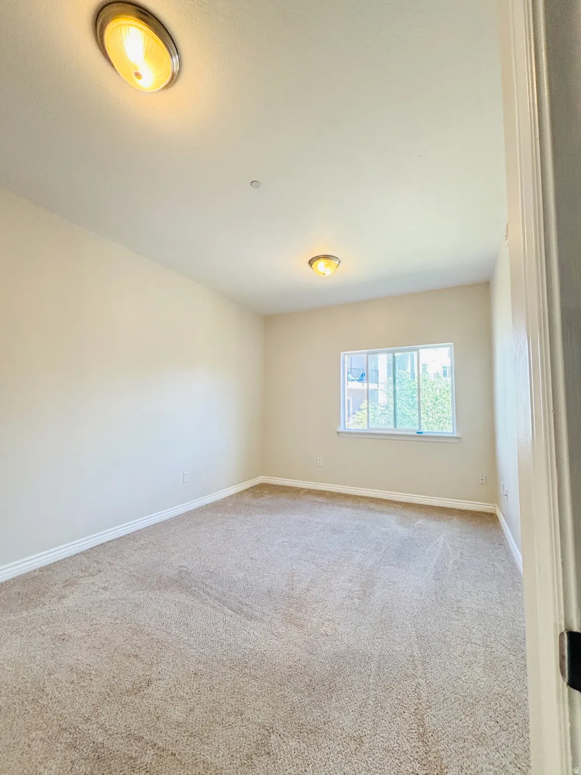 Carpeted room with a single window and two ceiling-mounted light fixtures