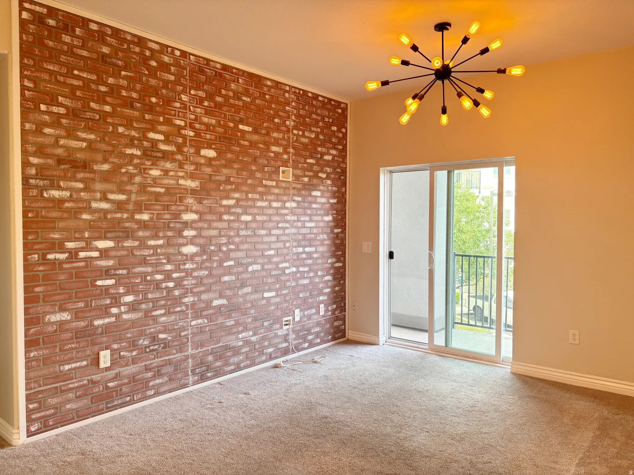 Exposed brick accent wall, modern sputnik chandelier, light neutral-toned walls, sliding glass door, and a private balcony with metal railings
