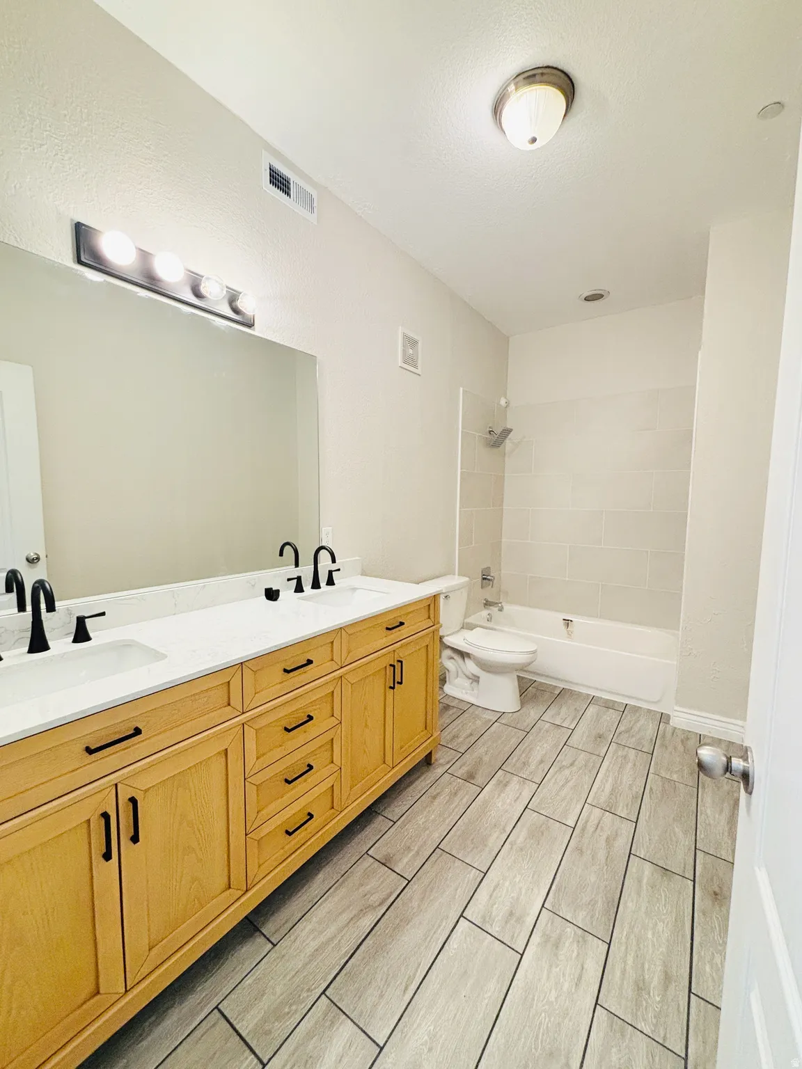 Dual sink vanity with light wood-finish cabinetry, white countertops, and matte black fixtures