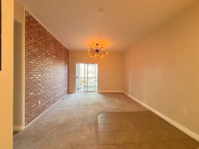 Exposed brick accent wall with a modern sputnik chandelier, carpet flooring, tile flooring, and sliding glass door