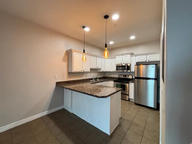 Kitchen featuring white cabinetry, granite-finish countertops, stainless steel appliances, and pendant lighting