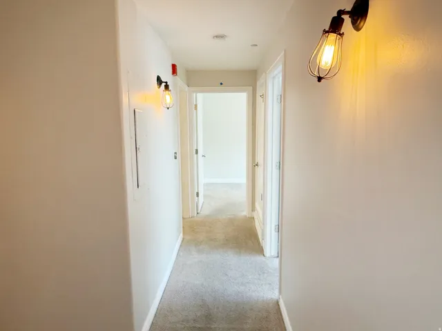 Hallway with light gray wall paint and matching carpeting, featuring two modern industrial style wall sconces and white trim