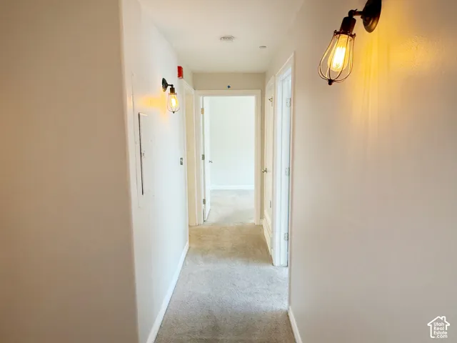 Hallway with light gray wall paint and matching carpeting, featuring two modern industrial style wall sconces and white trim