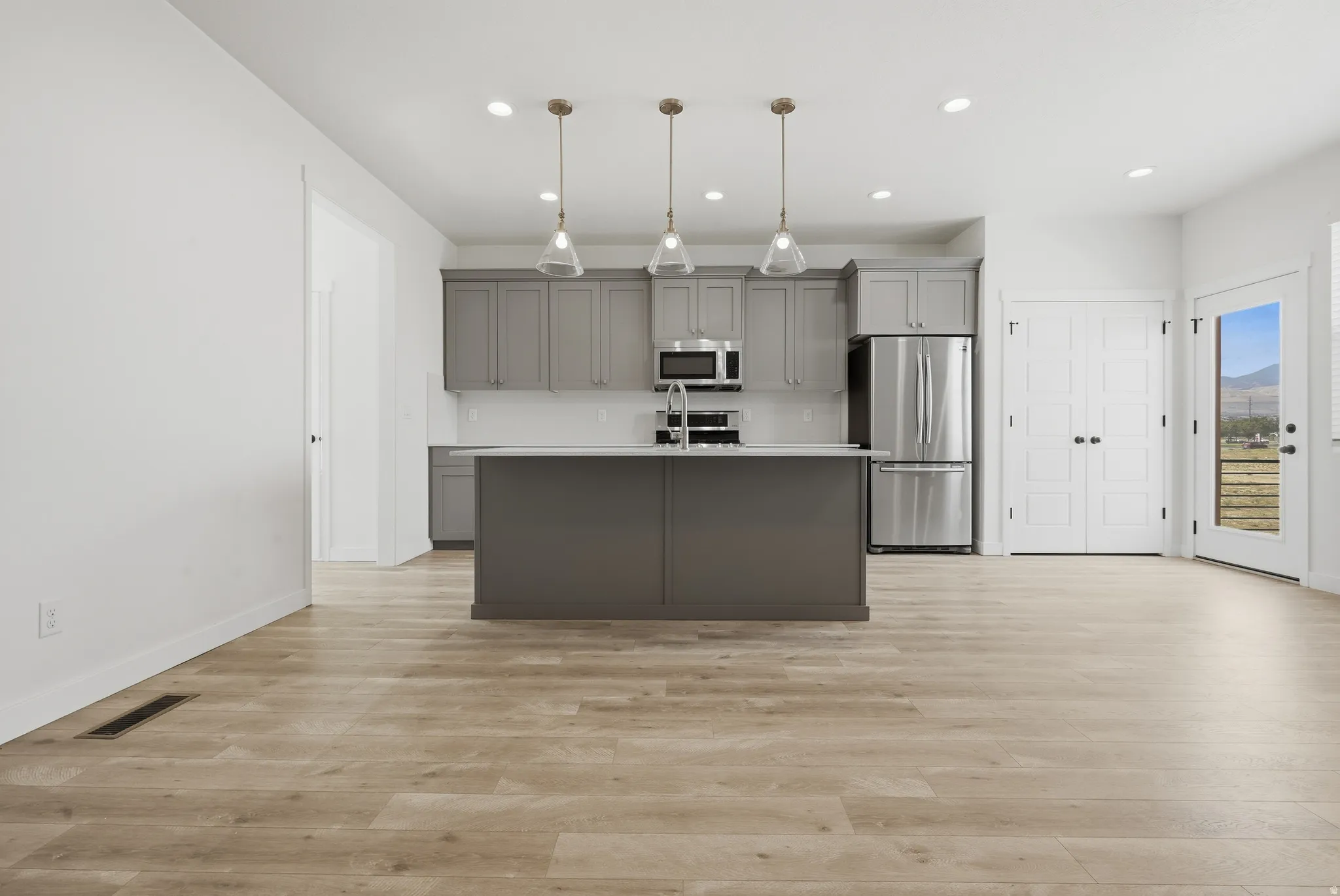 Kitchen featuring grey cabinetry, stainless steel appliances, a central island, and wood-finish flooring