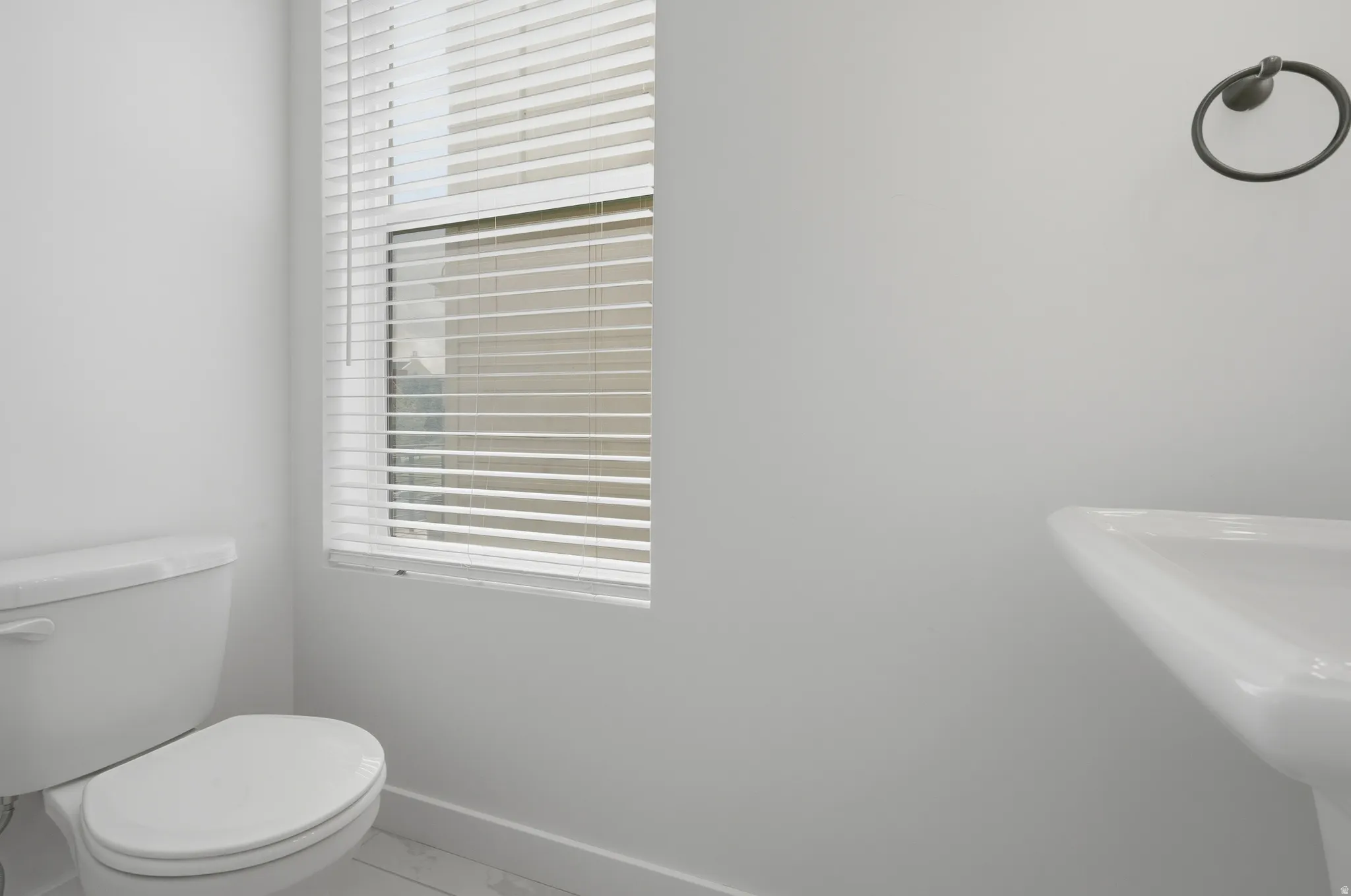 White ceramic toilet, pedestal sink, and window with horizontal blinds