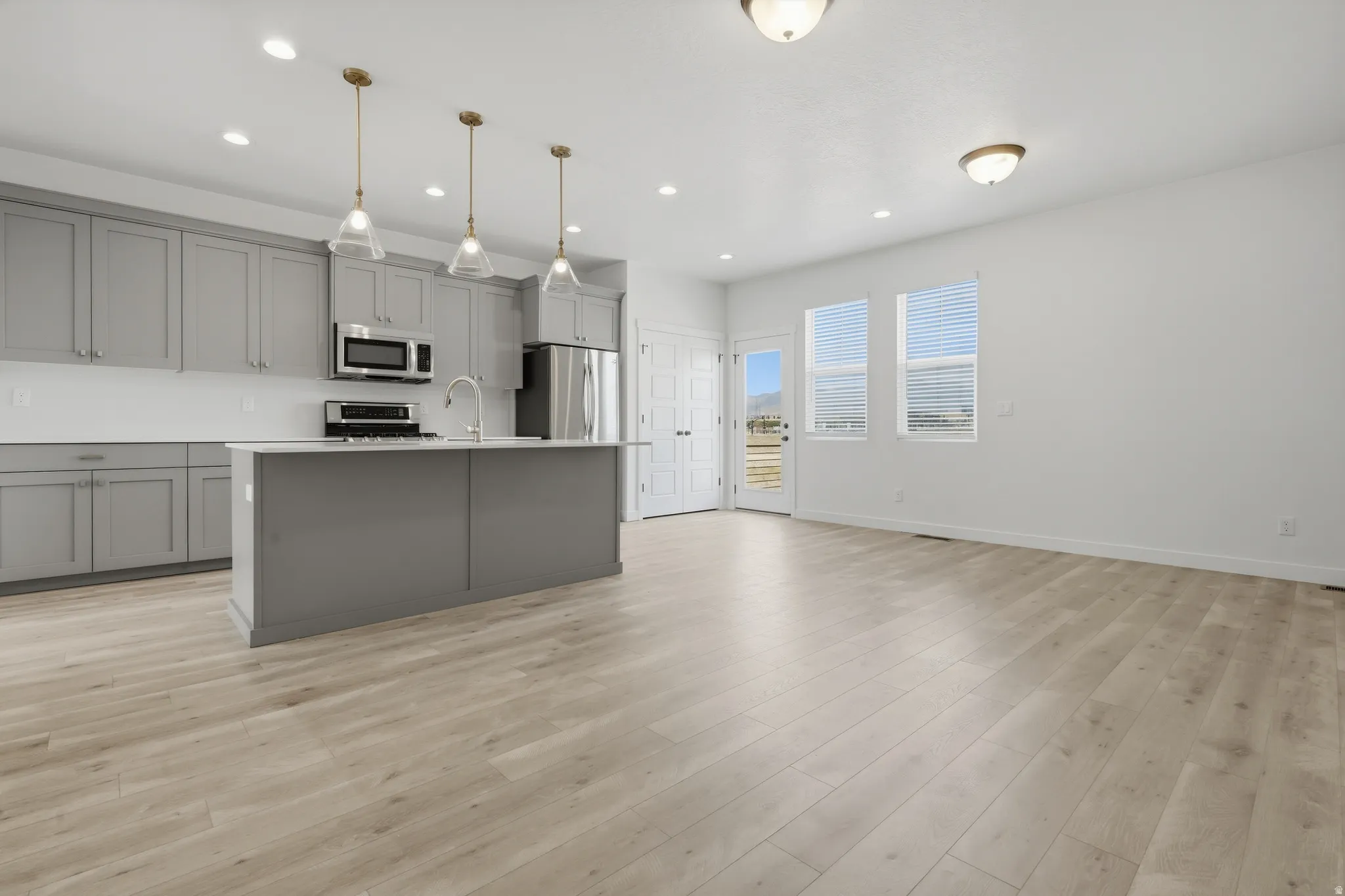 Modern kitchen featuring gray cabinetry, stainless steel appliances, a center island with sink, and pendant lighting