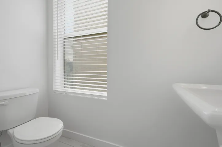White ceramic toilet, pedestal sink, and window with horizontal blinds