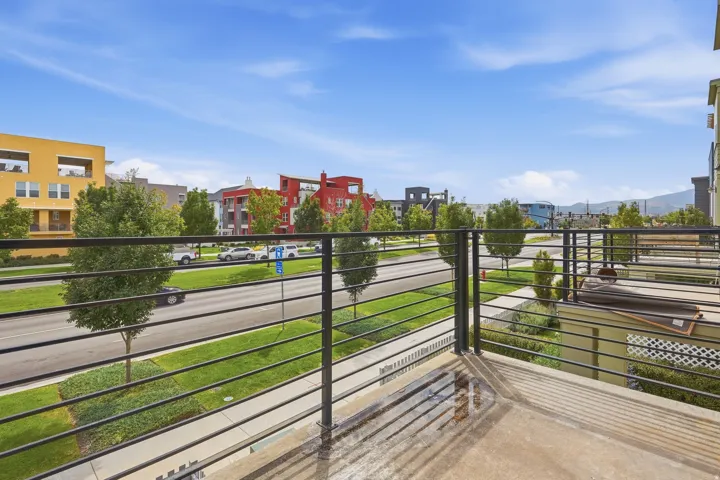 Concrete balcony with black metal railings overlooking a street with trees and buildings