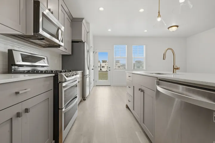 Contemporary kitchen featuring light gray cabinetry, stainless steel appliances, a center island with sink, light-toned wood-finish flooring, and recessed lighting
