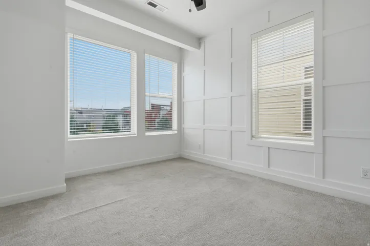 Neutral-toned carpeting, multiple windows with blinds, and decorative wall paneling