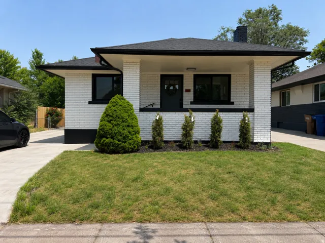 White brick exterior with black trim, concrete driveway, front porch with black railing, and manicured lawn