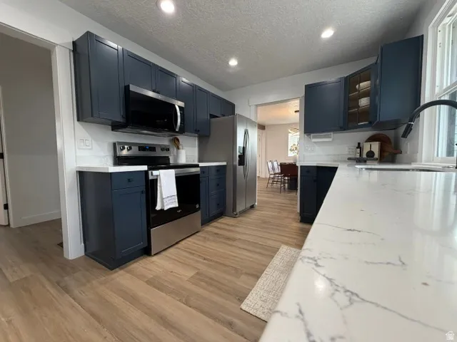 White countertops, stainless steel appliances, wood-finish flooring, recessed lighting, and dark blue cabinetry
