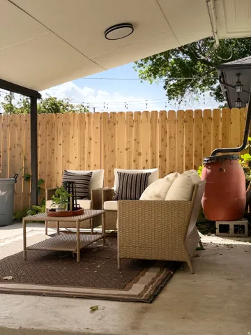 Covered patio with a concrete surface, wood privacy fence, and an exterior light fixture