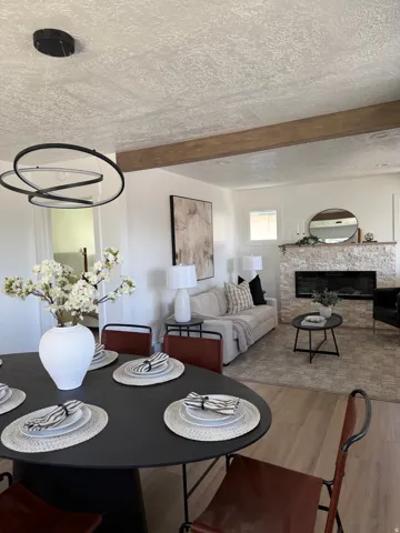 Open-concept living area featuring a stone-clad fireplace, wood-finish flooring, and exposed ceiling beams