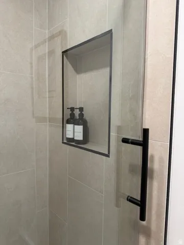 Tiled shower enclosure featuring a recessed niche with black trim, a clear glass shower door, and a matte black bar handle