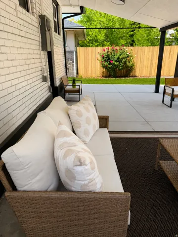 Covered patio featuring a concrete floor, dark support beams, and a white brick exterior