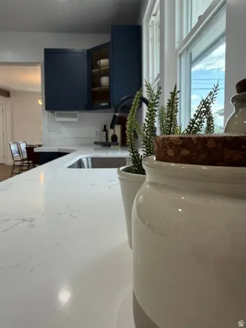 White countertops with subtle veining, dark blue cabinetry, and a stainless steel sink with a black faucet