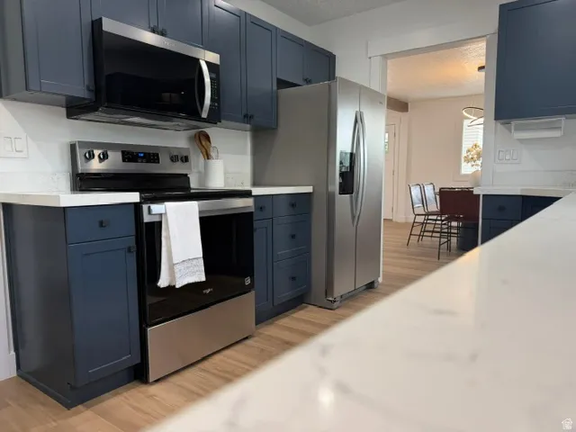 Navy blue cabinetry with matte black hardware, stainless steel appliances, light wood-finish flooring, white countertops, and white subway tile backsplash