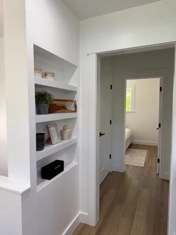 Built-in shelving, wood-finish flooring, white trim, and a white door with black hardware