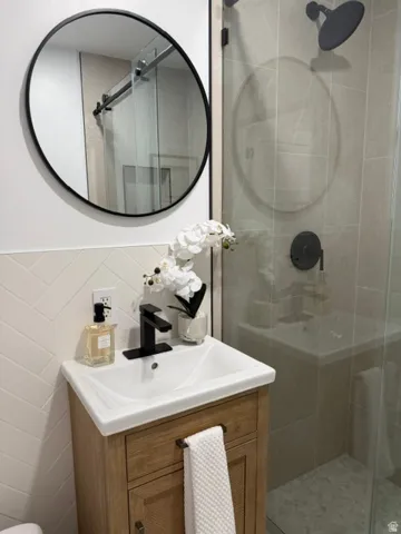 Herringbone tile wainscoting, a wall-mounted round mirror, and a wood-finish vanity with an integrated sink