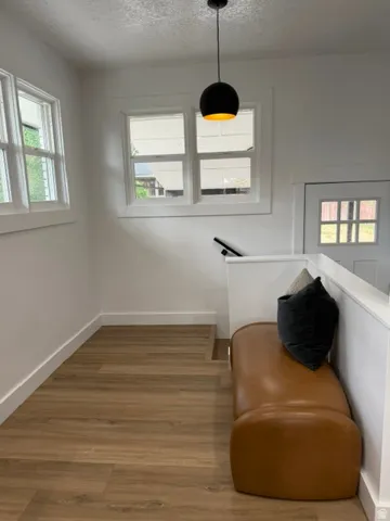 Multiple windows with white trim, wood-finish flooring, and a contemporary pendant light fixture