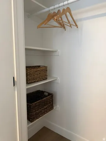 Built-in closet with a hanging rod, two storage shelves, and wood-finish flooring